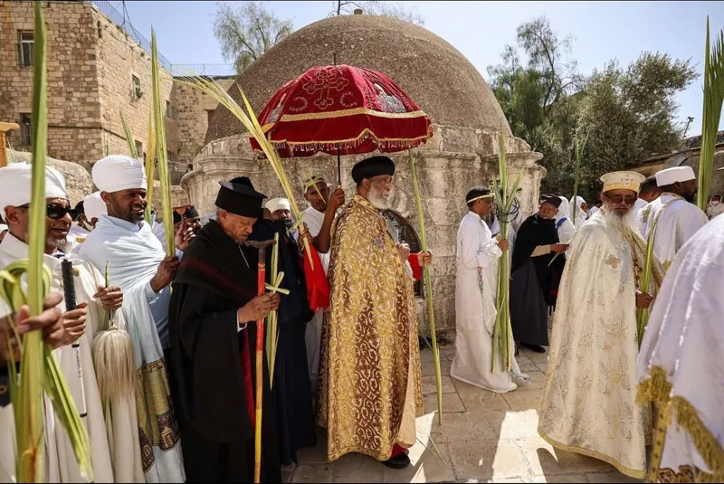 የዘንባባ ዝንጣፊ የያዙ የኢትዮጵያ ኦርቶዶክስ ካህናት እና ምዕመናን በቀይ የክብር ጥላ ሥር